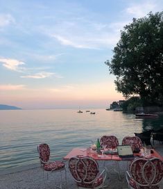 an outdoor dining table with red chairs next to the water