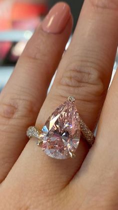 a close up of a person's hand holding a ring with a pink diamond