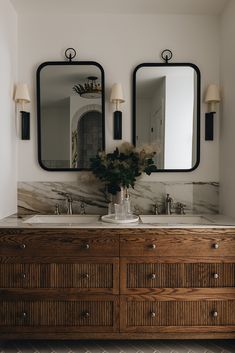 a bathroom with two large mirrors above the sinks and wooden cabinets below it, along with vases on either side of the sink