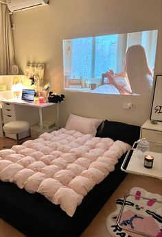 a room with a bed and a projector screen on the wall, in front of a window