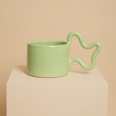 Handcrafted from stoneware clay, this mint green ceramic mug with distinctive wiggle handle is ideal for your morning coffee or afternoon tea. The quirky handle provides a playful aesthetic whilst also being ergonomic to hold. The Green Wiggle Mug will make a unique addition to your home and add a touch of joy to the everyday. Available in a range of colours, perfect for mixing and matching!  - Blue - Chartreuse - Mint Green - Orange - Pink 7cm high x 8cm wide Handmade in the UK. All pieces are entirely handmade in small batches from our East London studio. This means that some variations may occur, making each piece totally unique and special. Microwave and dishwasher safe, however I would recommend hand washing where possible. Funky Mug, Mug Handles, Morning Coffee Cups, British Gifts, Playful Aesthetic, Pretty Mugs, Green Mugs, Ultimate Gift Guide, Colorful Ceramics