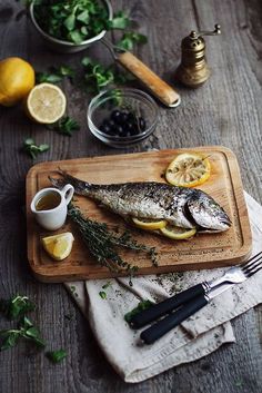 a fish is on a cutting board with lemons and olives next to it