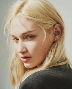 a woman with long blonde hair and piercings on her ears looking at the camera