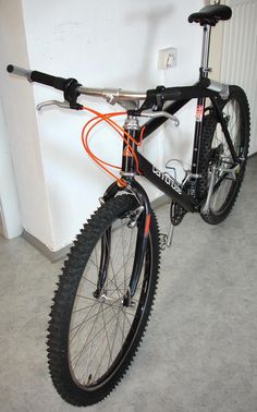 a black and orange bike parked next to a white wall