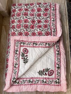 a pink and white quilt with flowers on it sitting on the floor next to a door