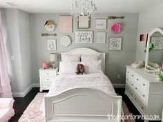 a white bed sitting in a bedroom next to a dresser and window with pink curtains