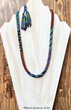 a necklace made with multicolored seed beads and tassels on a wooden stand