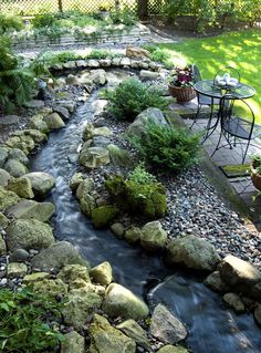 a small river running through a garden next to a table with chairs and tables on it