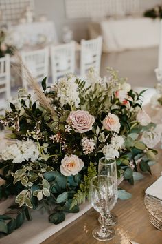 the table is set with white and pink flowers, greenery, and wine glasses