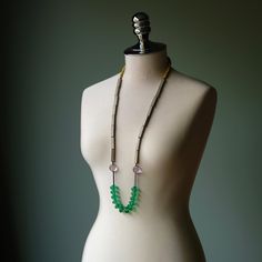 a white mannequin with a green beaded necklace on it's neck