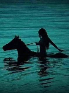 a woman riding on the back of a horse in water at night with her legs spread out