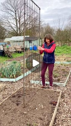 a woman standing in the middle of a garden holding onto a metal cage with plants growing out of it