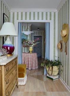 a hallway with striped walls and wooden flooring is decorated in pastel colors, along with potted plants on either side of the door