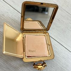 an open compact mirror on top of a wooden table next to a gold plated object