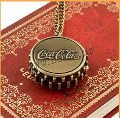 a coca cola bottle cap necklace sitting on top of a red book with gold trim