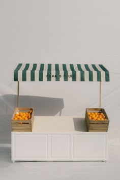 two wooden boxes with oranges under a green and white striped awning over them