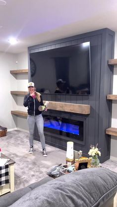 a woman standing in front of a flat screen tv next to a couch and fireplace