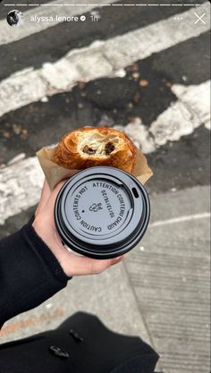 a person holding a pastry in their hand on the side of the road with a coffee cup next to it