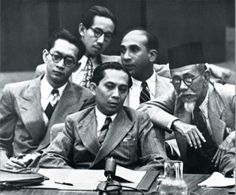 a group of men in suits and ties sitting at a table with papers on it