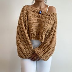 a woman is wearing a brown sweater and white pants with her hands on her hips