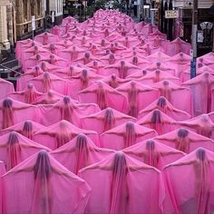 a large group of pink cloths are lined up on the street with buildings in the background