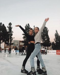 two people skating on an ice rink with trees in the backgroung and one person holding his arms up