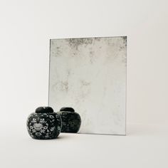 a black vase sitting next to a mirror on top of a white flooring area