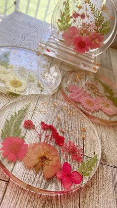 four glass plates with flowers on them sitting on a wooden table in front of a window