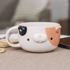 a coffee cup with a cat face on it and some crackers next to it