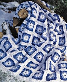 a blue and white crocheted blanket sitting on top of a pile of logs