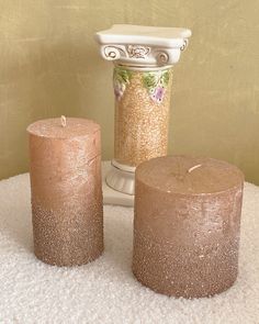 two candles sitting on top of a white rug next to a vase and candle holder