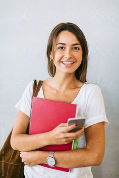 a woman holding a folder and a cell phone in her hand while smiling at the camera