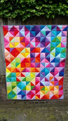 a multicolored quilt hanging on a brick wall next to a green planter