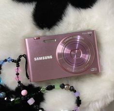 a pink camera sitting on top of a white fur covered floor next to a necklace