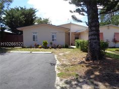 a house that is in the middle of a driveway with trees and bushes around it