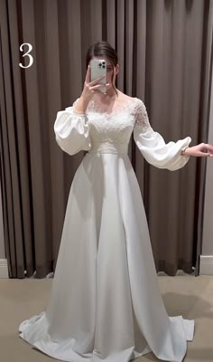 a woman taking a selfie wearing a white wedding dress with long sleeves and an open back