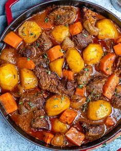 beef stew with carrots and potatoes in a red pot on a blue tablecloth