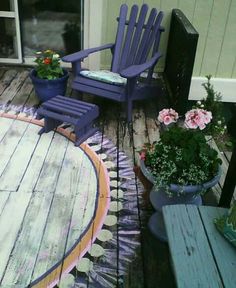 two purple chairs sitting on top of a wooden deck next to flowers and potted plants