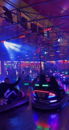 two people riding bumper cars in an indoor area with colorful lights on the ceiling and floor