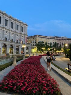 a woman is walking down the sidewalk in front of a building with flowers on it