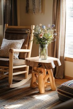 a wooden rocking chair next to a small table with flowers in a vase on it