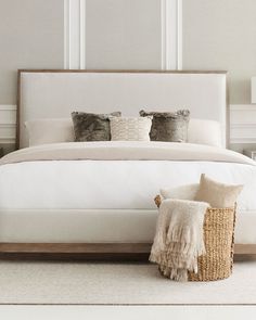 a bed with white linens and pillows in a neutral bedroom, along with a wicker basket on the floor