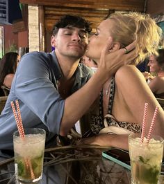 a man and woman kissing each other at a table with drinks in front of them