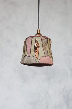 a lamp hanging from a ceiling with a white wall in the back ground and a light on top of it