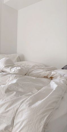 an unmade bed with white sheets and pillows