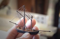 a hand holding a small model ship in it's left hand, with the sails down