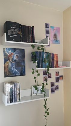 a white shelf with books and pictures on it next to a plant in a vase