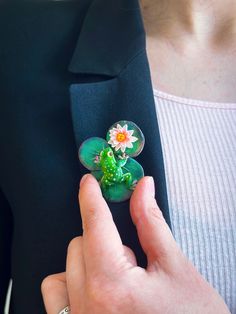 a close up of a person's hand holding a brooch with a flower on it