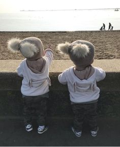 two young children standing next to each other near the ocean with their arms in the air