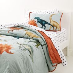 a child's bed with dinosaur comforter and pillowcases on the headboard